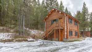 Eine Blockhütte mit einer Holztreppe, die zu einem Balkon führt, umgeben von verschneiter Landschaft und dichtem Wald.