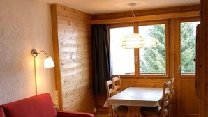 A cozy room with a wooden interior, a dining table with chairs, a red sofa, and a window with a view of trees.