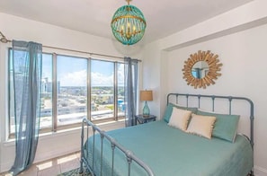 A bedroom with a bed, a view of the city, a chandelier, and a wall clock.
