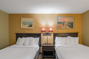A hotel room with two beds, a nightstand with a lamp, and two paintings on the wall.