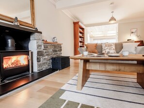 A cozy living room with a stone fireplace, a wooden table with a book and a cup, and a bookshelf filled with books. - 3 bedroom accommodation in Aberfeldy (Aberfeldy)
