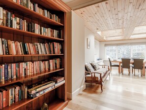 A room with a large wooden bookshelf filled with books, a wooden dining table with chairs, and a window with a view of the outside.