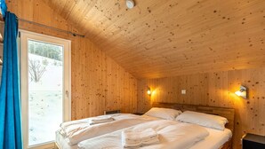 A wooden cabin bedroom with two beds, a window with curtains, and a nightstand.