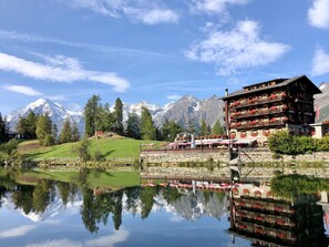 A hotel with a reflection in a lake, surrounded by mountains and trees.