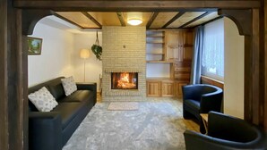 Een gezellige woonkamer met een open haard, een bank, een fauteuil en een klein vloerkleed.