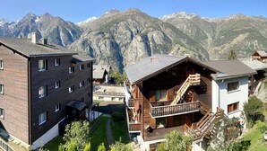 Een berghut met houten architectuur, een balkon en uitzicht op besneeuwde bergen.