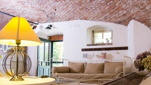 A cozy room with a brick ceiling, a white sofa with cushions, a small table with a lamp, and a window with a view of greenery. - Lovely apartment for 4 people with pool, WIFI and patio (Zábreh)
