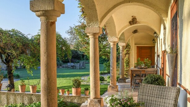 A covered outdoor area with stone columns, a round table with chairs, and potted plants. - Lovely apartment for 4 people with pool, WIFI and patio (Zábreh)