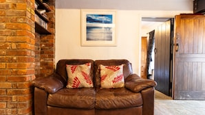 A brown leather sofa with leaf-patterned cushions, a brick wall, a framed picture, and a wooden door.