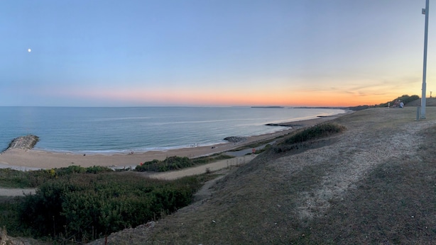 A coastal landscape with a clear sky, a beach, and a rocky outcrop.