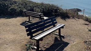 A bench overlooking a beach with a clear view of the ocean and distant hills.