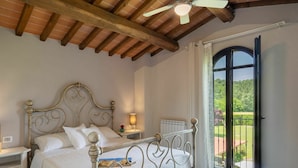 A bedroom with a bed, nightstands, a ceiling fan, and a view of a garden through a door. - Wonderful private villa for 4 guests with pool, WIFI, TV and pets allowed (Terranuova Bracciolini)