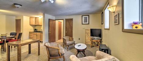 Sala de estar con una mesa de comedor, sillas, sofá, televisor y una cocina al fondo.