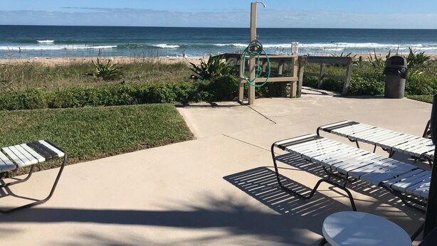 Eine Terrasse am Strand mit Liegestühlen und einem kleinen Tisch, mit Blick auf den Ozean.