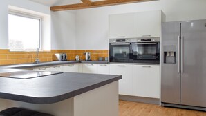 Una cocina moderna con armarios blancos, una encimera gris, horno empotrado, refrigerador de acero inoxidable y una ventana sobre el fregadero.