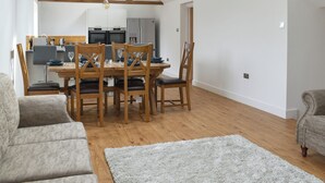 Amplia sala de estar con una mesa de comedor de madera, sillas y un sofá. Se observa una cocina con electrodomésticos modernos al fondo.