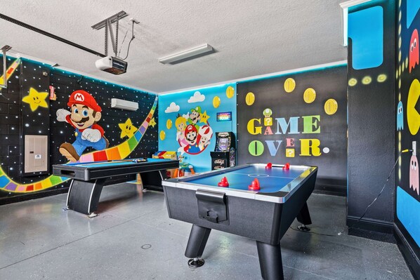 Ein Raum mit zwei Tischfußballtischen, einem Projektor und einer Wand mit Mario und Luigi.