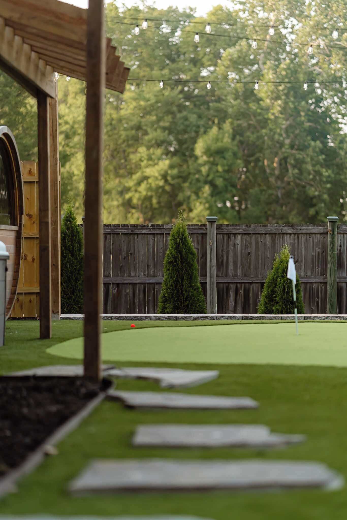 A miniature golf course with a wooden pergola, a wooden fence, and a backdrop of trees.