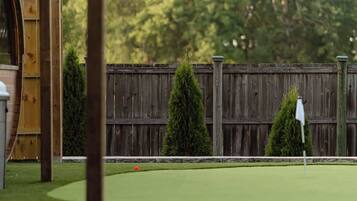 A miniature golf course with a wooden pergola, a wooden fence, and a backdrop of trees.