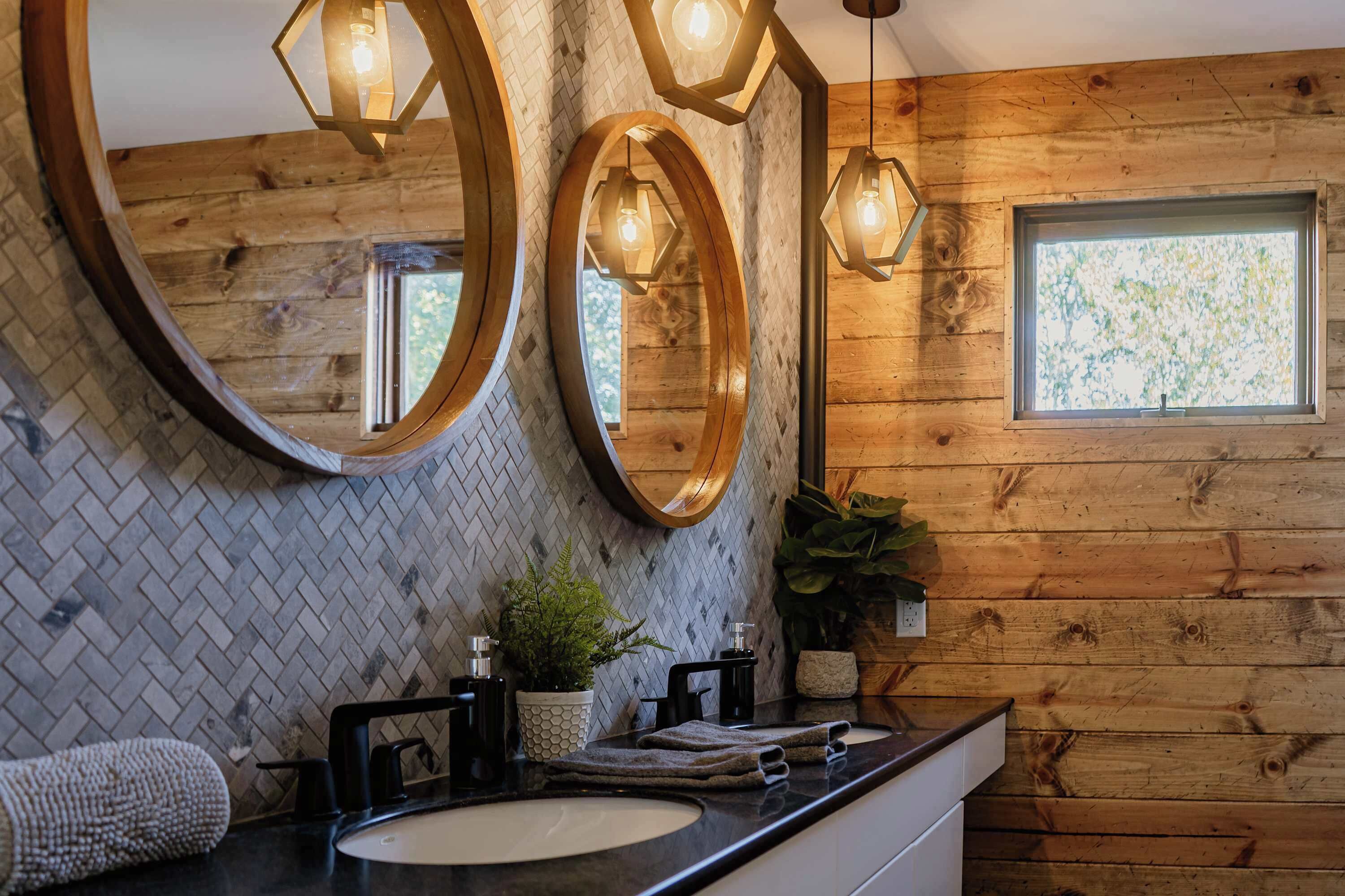 A bathroom with wooden walls, a herringbone tile backsplash, a large mirror, and a window with a view of trees.