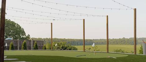 A well-maintained lawn with a putting green, wooden posts, and string lights.