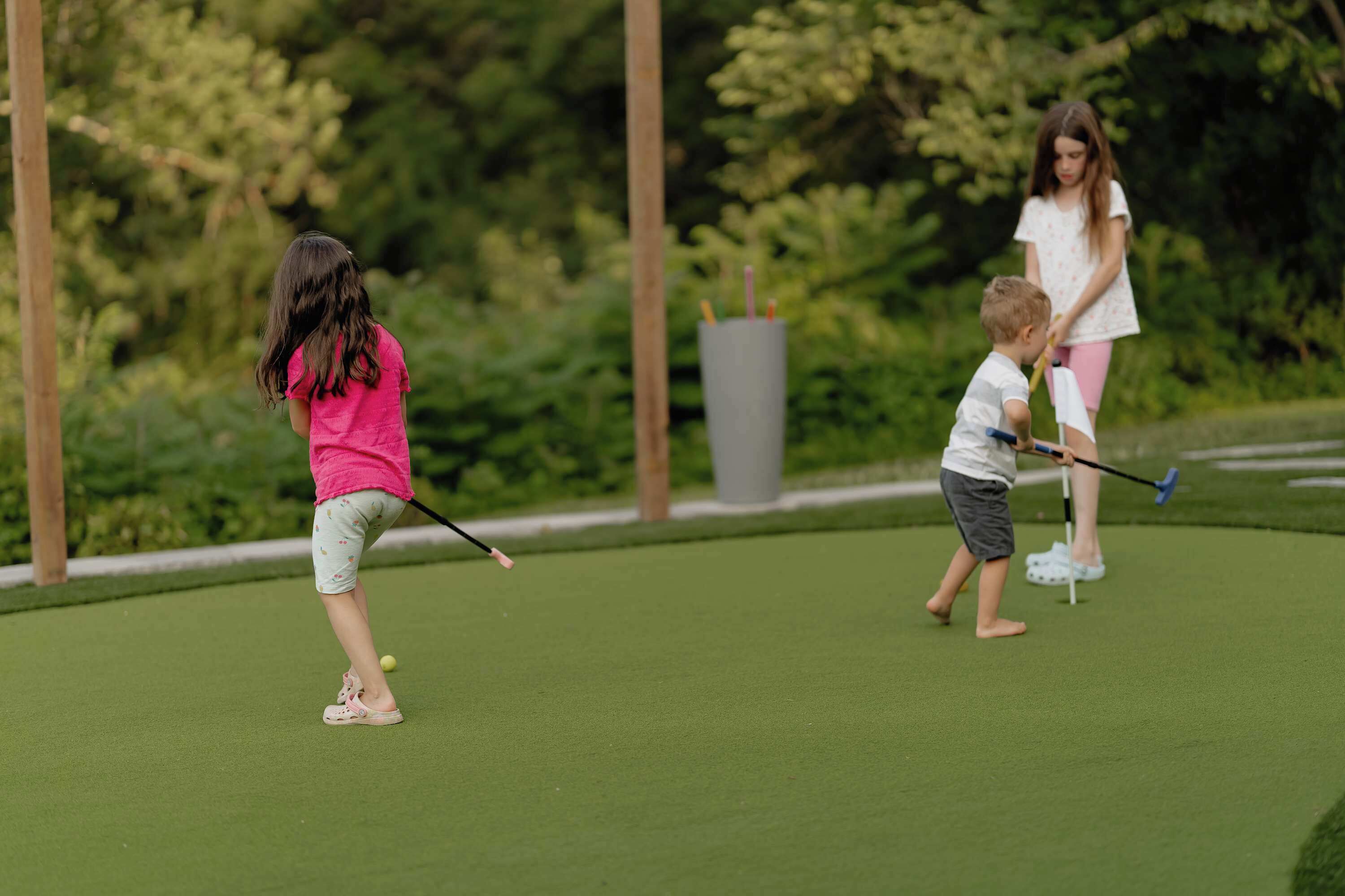 Een kind en een volwassene spelen golf op een groen veld, met bomen op de achtergrond.