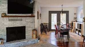 Una sala de estar con chimenea, televisor montado en la pared y un comedor con sillas y mesa.