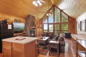 Un interior de cabaña espacioso con chimenea de piedra, muebles de madera y ventanas amplias que ofrecen vistas al exterior.