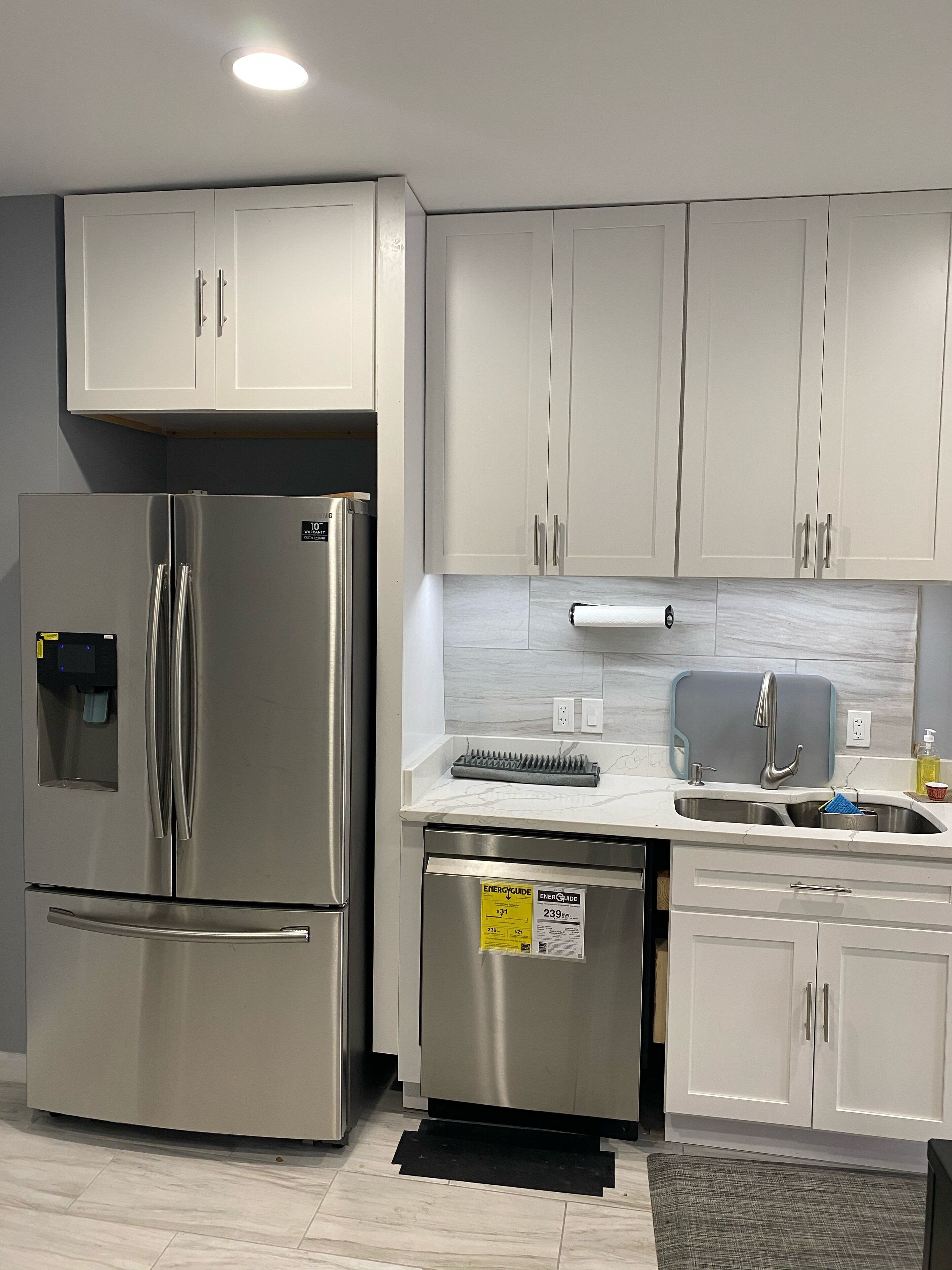 A modern kitchen with stainless steel appliances, white cabinetry, and a built-in dishwasher.