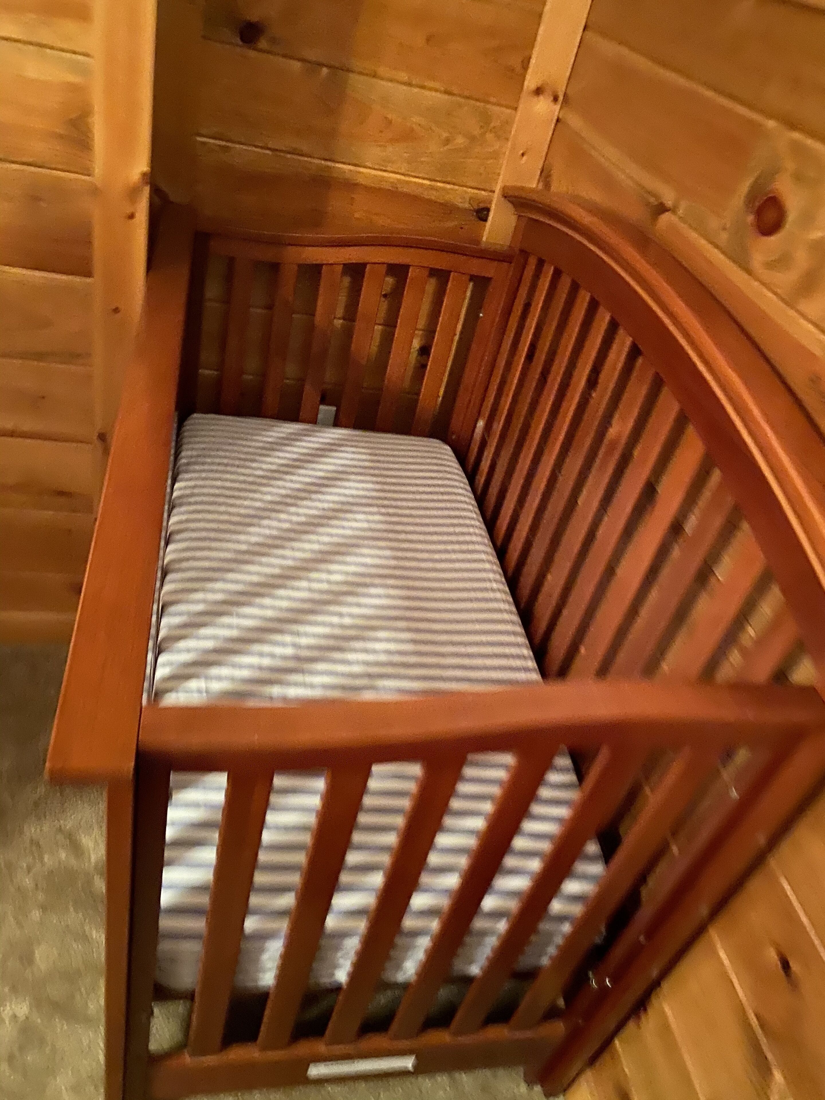 A wooden crib with a striped mattress in a log cabin room.