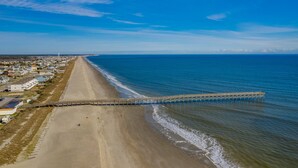 Een strand met een steiger die zich uitstrekt over de oceaan, omringd door woongebouwen.
