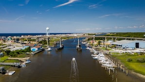 Een jachthaven met aangemeerde boten, een brug erboven en een vuurtoren in de verte.