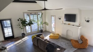 Ein geräumiges Wohnzimmer mit einem großen Sofa, einem gelben Hocker und einem an der Wand montierten Fernseher.