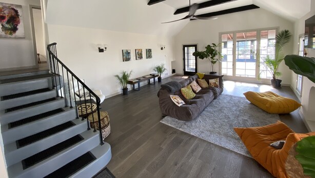Ein geräumiger Wohnbereich mit Treppe, einer großen Couch und einem Deckenventilator.