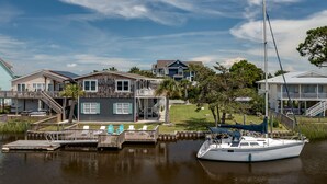 A waterfront property with a dock, a sailboat, and a house with a balcony overlooking the water.