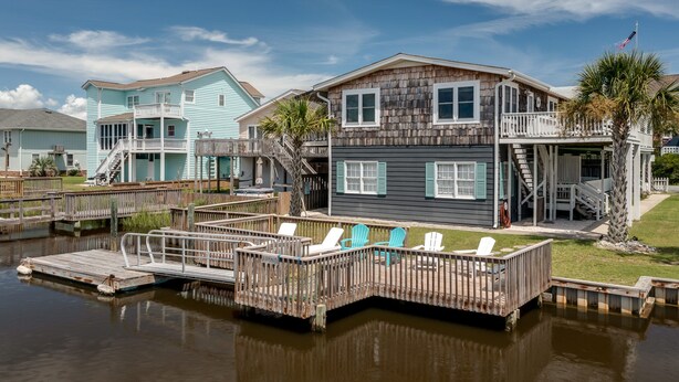 A waterfront property with a dock, a covered deck, and a two-story house with a balcony.