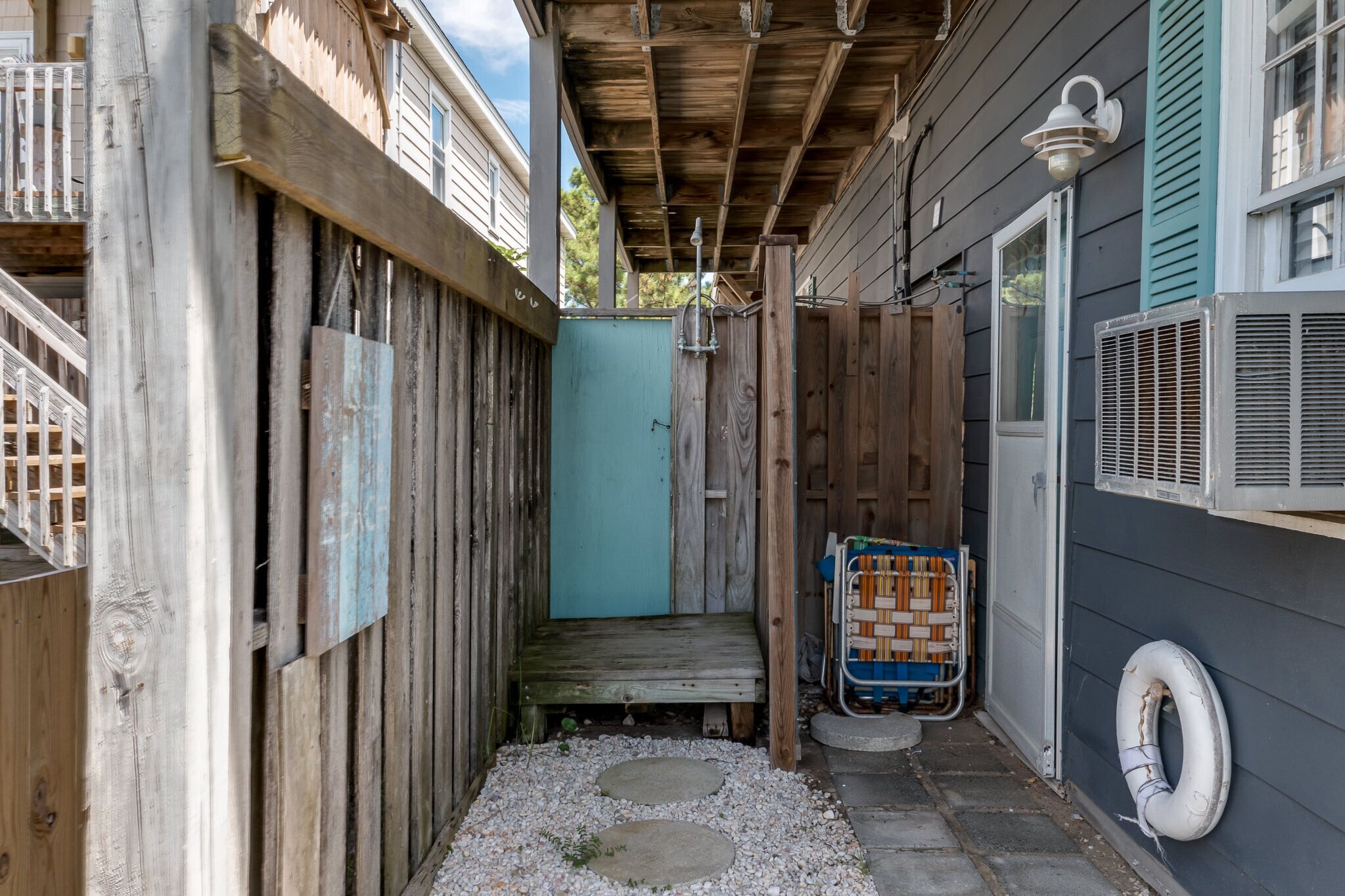 A narrow outdoor space with a wooden deck, a blue door, and a small step leading to a covered area.