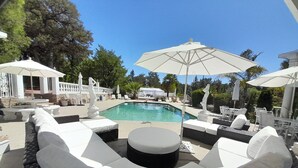 Un espace aménagé au bord de la piscine, avec des chaises longues blanches, une table ronde et des parasols.