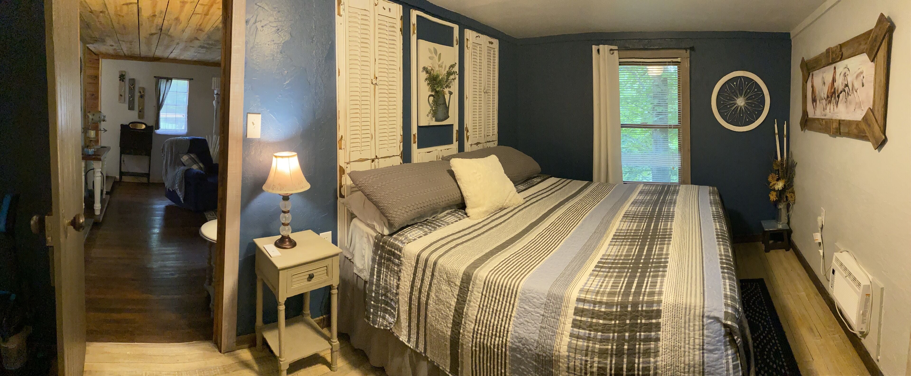 Une chambre à coucher avec un grand lit, une table de chevet avec une lampe, une fenêtre avec des stores et une horloge murale.