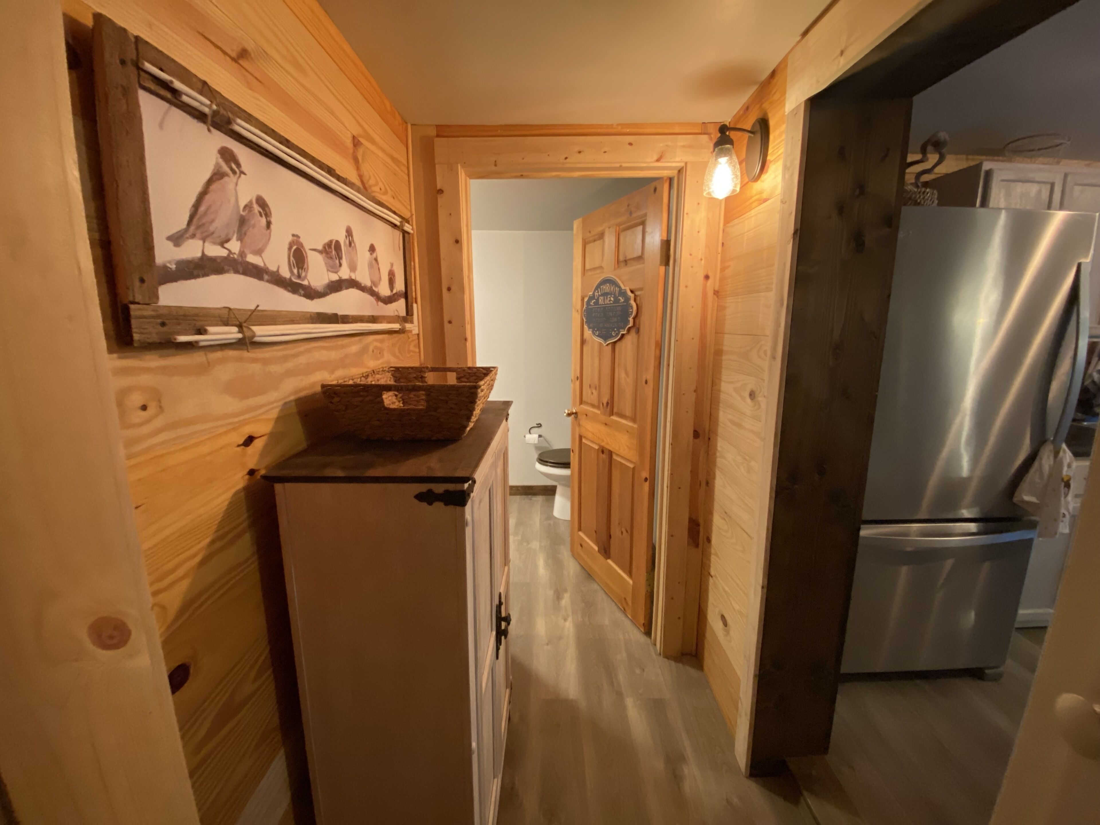 A wooden interior with a refrigerator, a basket on a counter, and a door with a sign.