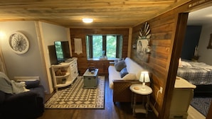 A cozy cabin interior with a wooden ceiling, a sofa, a television, and a small table with a lamp.