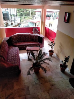 A balcony with a red and beige color scheme, featuring a sofa, a small round table, and several potted plants. - Ravine inn (Dharamshala)