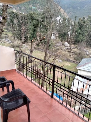 A balcony with a view of a mountainous landscape, featuring trees and a small building. - Ravine inn (Dharamshala)