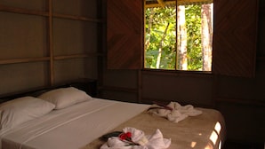 A room with a bed, a window with curtains, and a view of greenery outside.