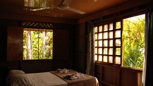A bedroom with a bed, a ceiling fan, and a window with a view of greenery.