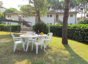 A round table with four white chairs in a grassy outdoor area, a bottle of wine, and a vase with sunflowers. - Cozy Oasis for Families-beahost (San Michele al Tagliamento)