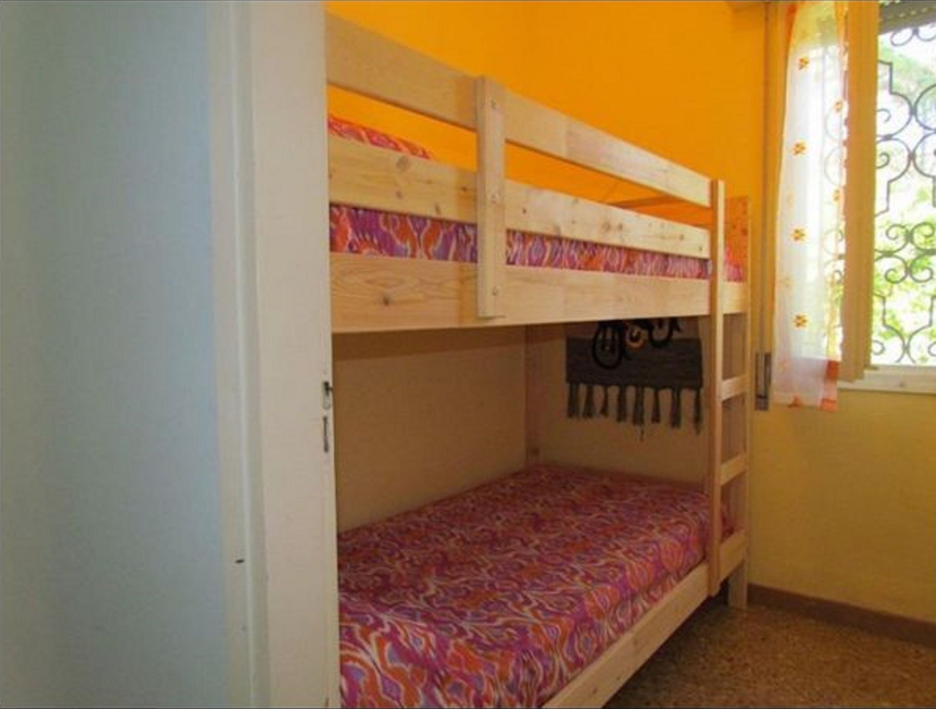 Una cama individual superpuesta con un colchón estampado en una habitación con paredes amarillas y una ventana con reja de metal.