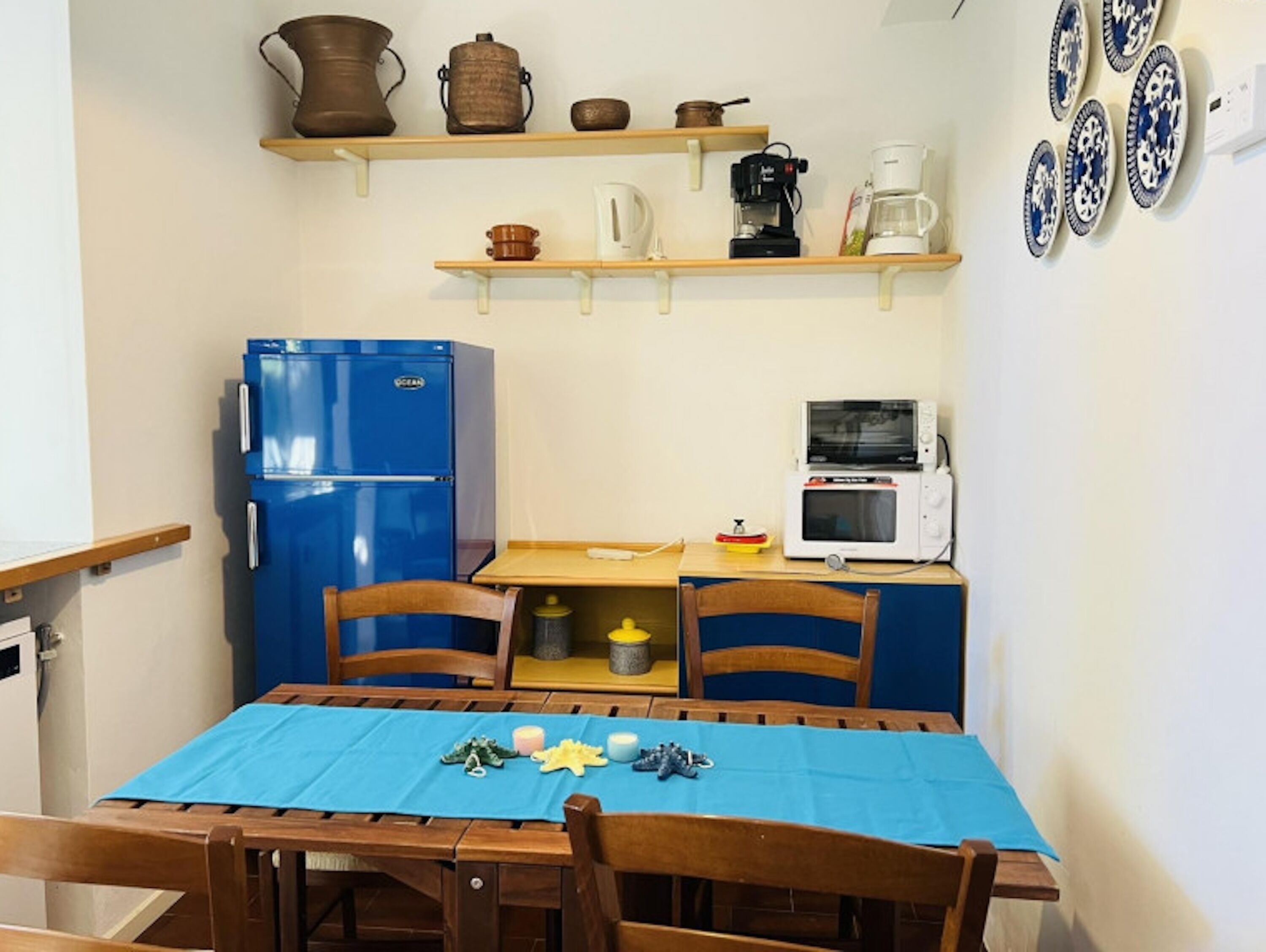 Una cucina compatta con un frigorifero blu, un forno a microonde e una macchina da caffè sul piano di lavoro.