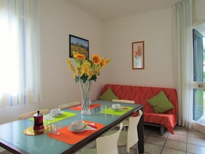 Un coin repas avec une table en verre, des chaises, un vase de fleurs et un canapé avec des coussins.