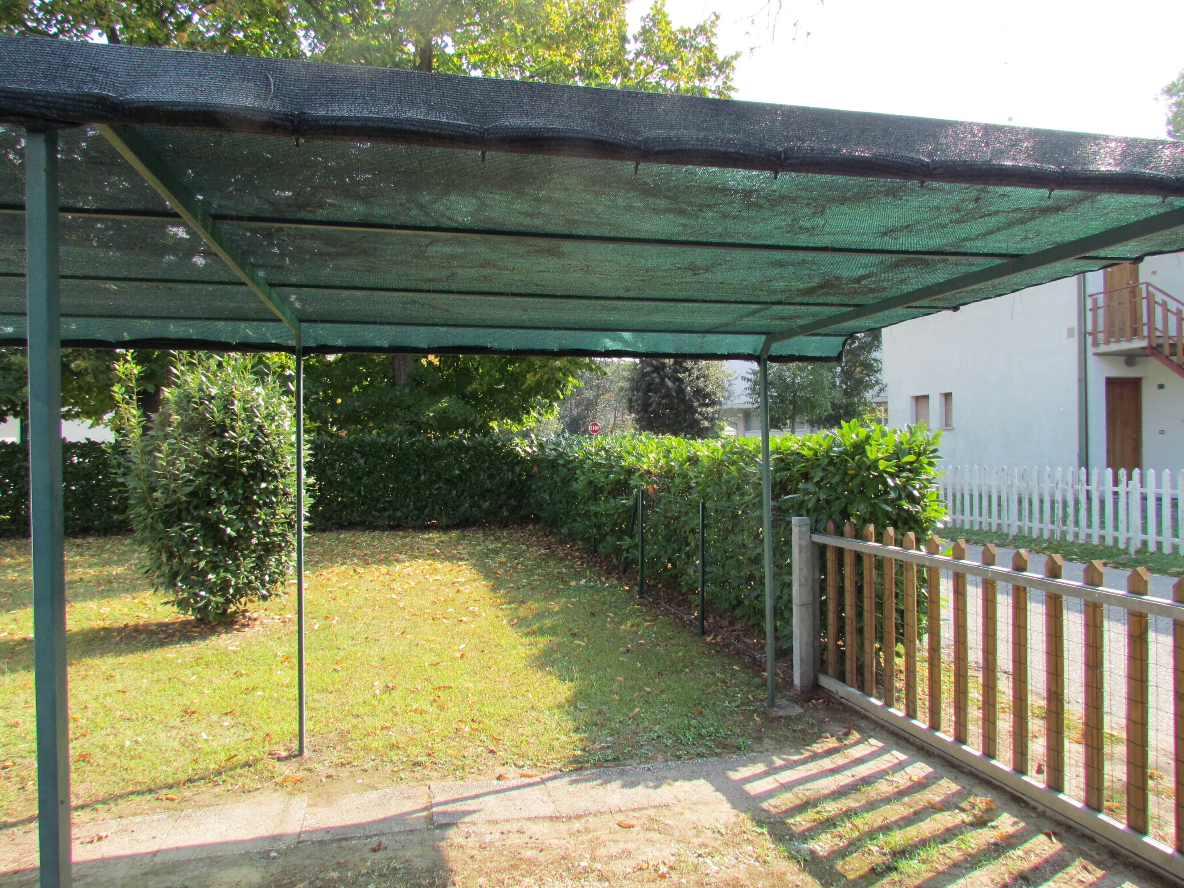 Un espace extérieur abrité, délimité par une clôture blanche, agrémenté de verdure, avec un bâtiment visible au fond.